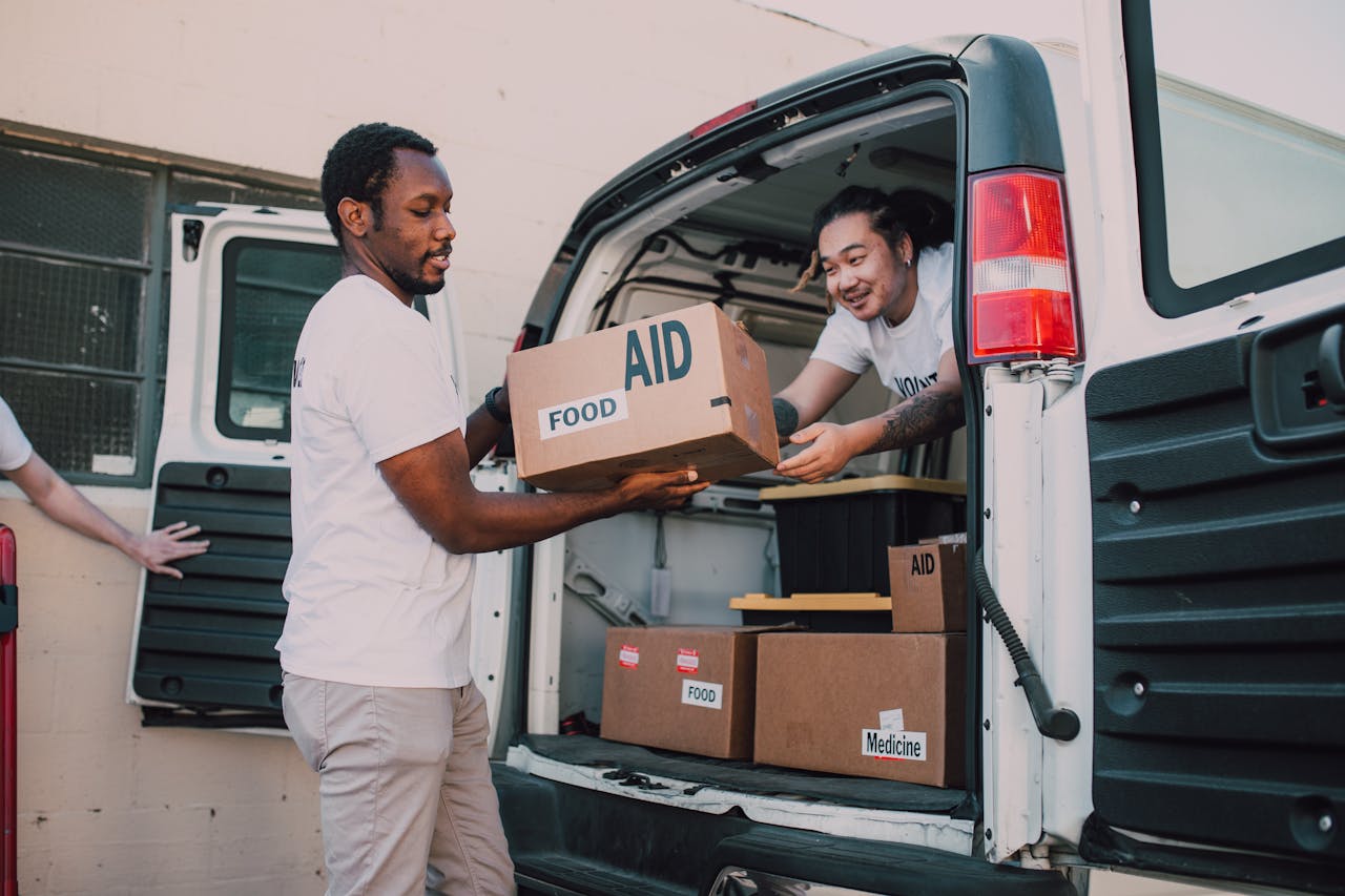 Two volunteers loading boxes labeled 'aid' into a van for community food donation drive.